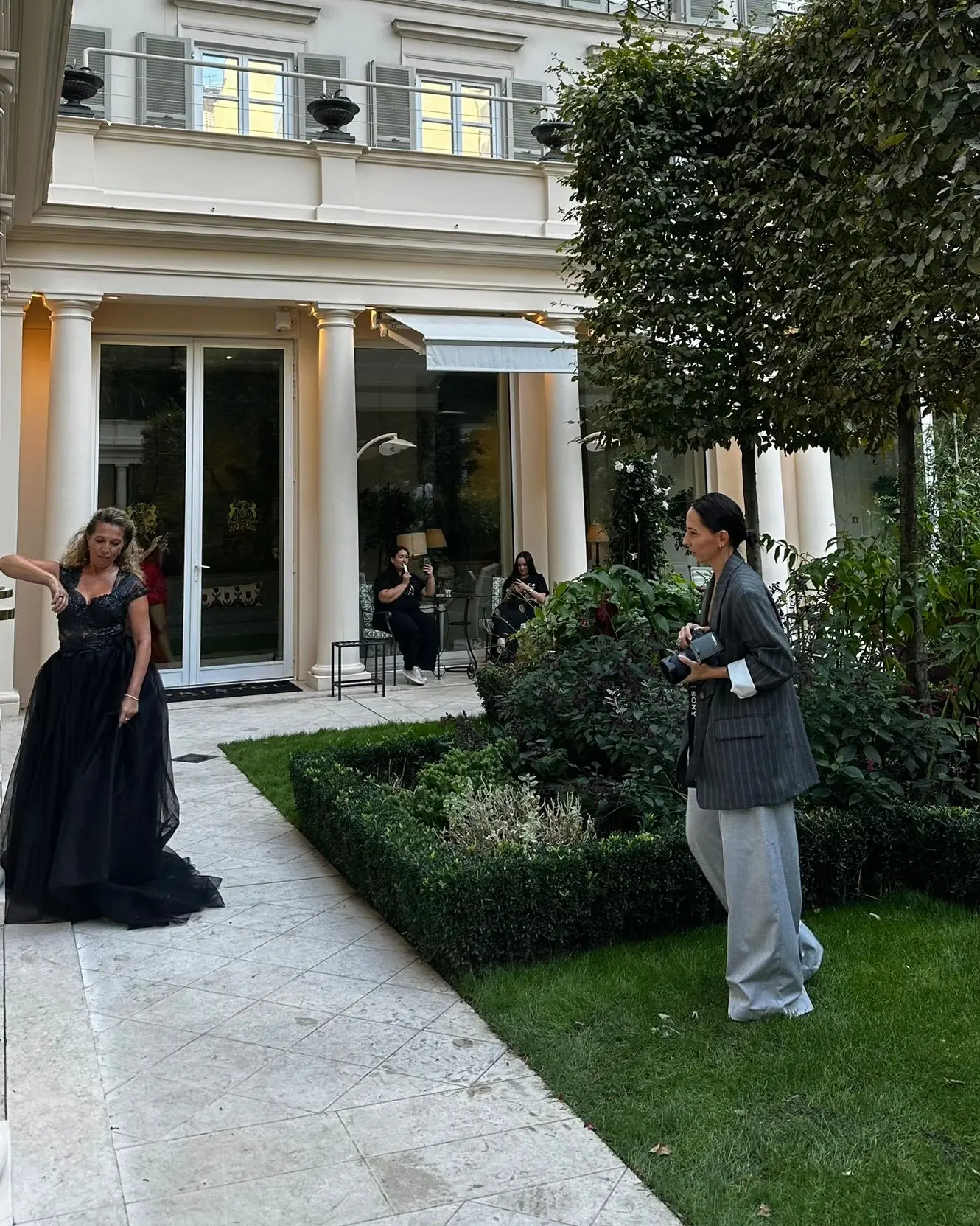 Photographe de profil qui photographie une mannequin en robe longue dans une cour