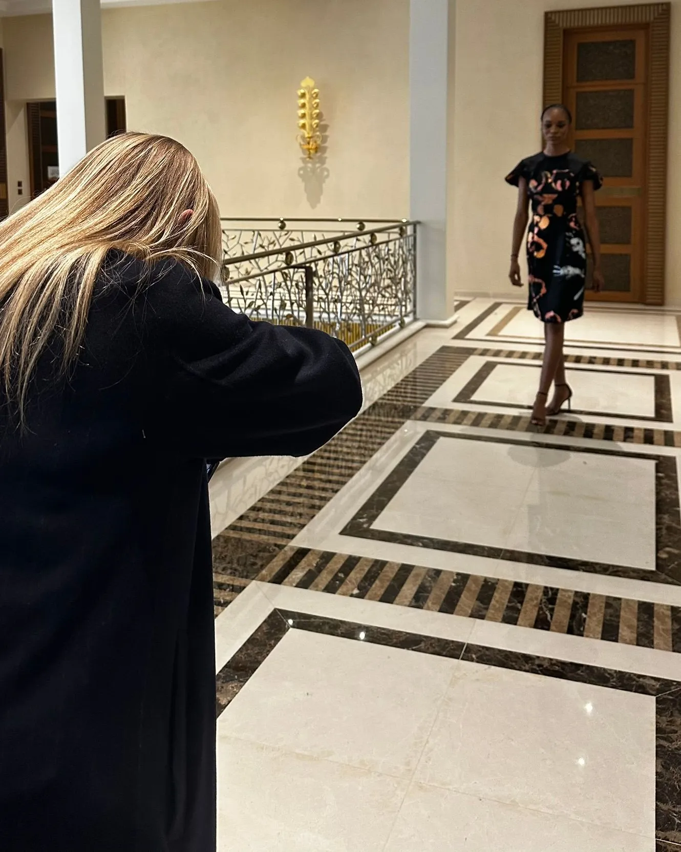 Photographe de dos qui photographie une mannequin dans un hall en marbre